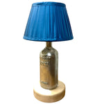 Load image into Gallery viewer, A table lamp featuring a metallic Absolut Vodka bottle as the base, topped with a blue pleated fabric lampshade and resting on a round light wood base, isolated on a white background.
