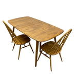 Load image into Gallery viewer, A mid-century modern wooden dining table set with two matching spindle-back chairs, shown on a solid white background.
