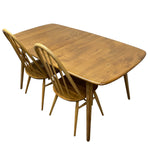 Load image into Gallery viewer, A mid-century modern wooden dining table with a rectangular shape and rounded corners, accompanied by two matching wooden spindle-back chairs, shown against a plain white background.
