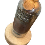 Load image into Gallery viewer, A vintage Absolut Vodka glass bottle mounted on a round light wood base, shown against a plain white background.

