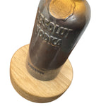 Load image into Gallery viewer, A vintage Absolut Vodka glass bottle mounted on a round light wood base, shown against a plain white background.
