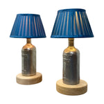 Load image into Gallery viewer, A pair of vintage-style table lamps featuring metallic silver bottle bases with gold-toned necks, blue pleated fabric shades, and round light wood bases, shown against a plain white background.
