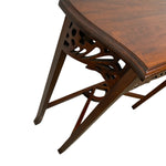 Load image into Gallery viewer, Close-up of a dark brown wooden table corner showing the tabletop, carved openwork leg support, and angled legs on a white background.
