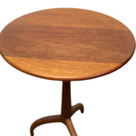 Load image into Gallery viewer, A round wooden side table with a warm medium-brown finish and a curved tripod pedestal base, shown against a plain white background.
