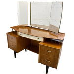 Load image into Gallery viewer, Mid-century modern wooden vanity desk with three angled mirrors, wood-grain finish, cream drawer fronts, and brass hardware, shown on a plain white background.

