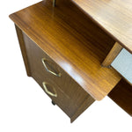 Load image into Gallery viewer, Close-up of a mid-century modern wooden desk with a warm brown walnut finish, featuring a pull-out drawer with brass handles and a light wood desktop shelf.

