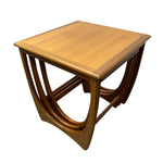 Load image into Gallery viewer, A mid-century modern wooden nesting side table with a warm honey-toned wood finish, featuring a square top and curved, multi-tiered base structure, shown on a plain white background.
