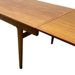 Load image into Gallery viewer, Close-up of a wooden extendable dining table with a warm medium-brown finish and visible wood grain, showing part of the tabletop, leg, and extension joint on a plain white background.
