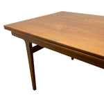 Load image into Gallery viewer, A mid-century modern wooden dining table with a warm medium-brown finish, featuring a visible leaf extension joint under the tabletop and a tapered leg, shown against a plain white background.
