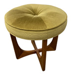 Load image into Gallery viewer, A round tufted ottoman stool with a textured mustard yellow fabric cushion and a mid-century modern wooden star base, shown on a plain white background.
