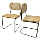 Load image into Gallery viewer, Two matching modern dining chairs with woven cane seats and backs and chrome cantilevered metal frames, shown on a plain white background.
