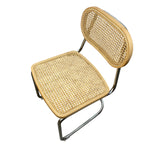 Load image into Gallery viewer, A modern side chair with a natural woven cane seat and backrest, supported by a curved polished chrome metal frame, shown on a solid white background.
