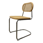 Load image into Gallery viewer, A modern cantilever dining chair with a woven cane seat and backrest, supported by a polished chrome tubular steel frame, shown against a plain white background.
