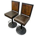 Load image into Gallery viewer, Two matching bar stools with distressed brown textured vinyl seats and backrests, black metal frames, and round swivel bases with footrests, shown on a white background.
