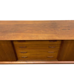 Load image into Gallery viewer, A mid-century modern wooden sideboard or credenza with a warm medium-brown wood grain finish, featuring a top surface and a central drawer section with six small drawers and dark metal pulls, shown against a plain white background.
