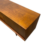 Load image into Gallery viewer, A close-up of a mid-century modern wooden sideboard or credenza, showing the warm honey-brown wood grain on the top surface and drawer fronts, isolated on a white background.
