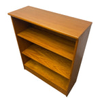Load image into Gallery viewer, A mid-century modern wooden bookcase with three shelves, made of warm honey-toned wood with a glossy finish, shown on a plain white background.
