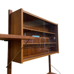 Load image into Gallery viewer, A mid-century modern wooden display cabinet with glass doors and shelves, mounted on a wall with a wooden shelf extending from the side, shown against a plain white background.
