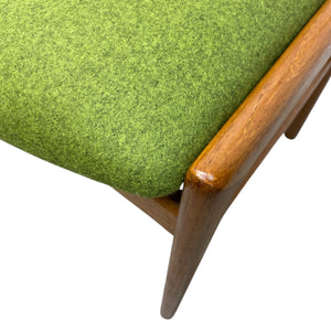 Close-up of a green upholstered chair with wooden armrest and leg.