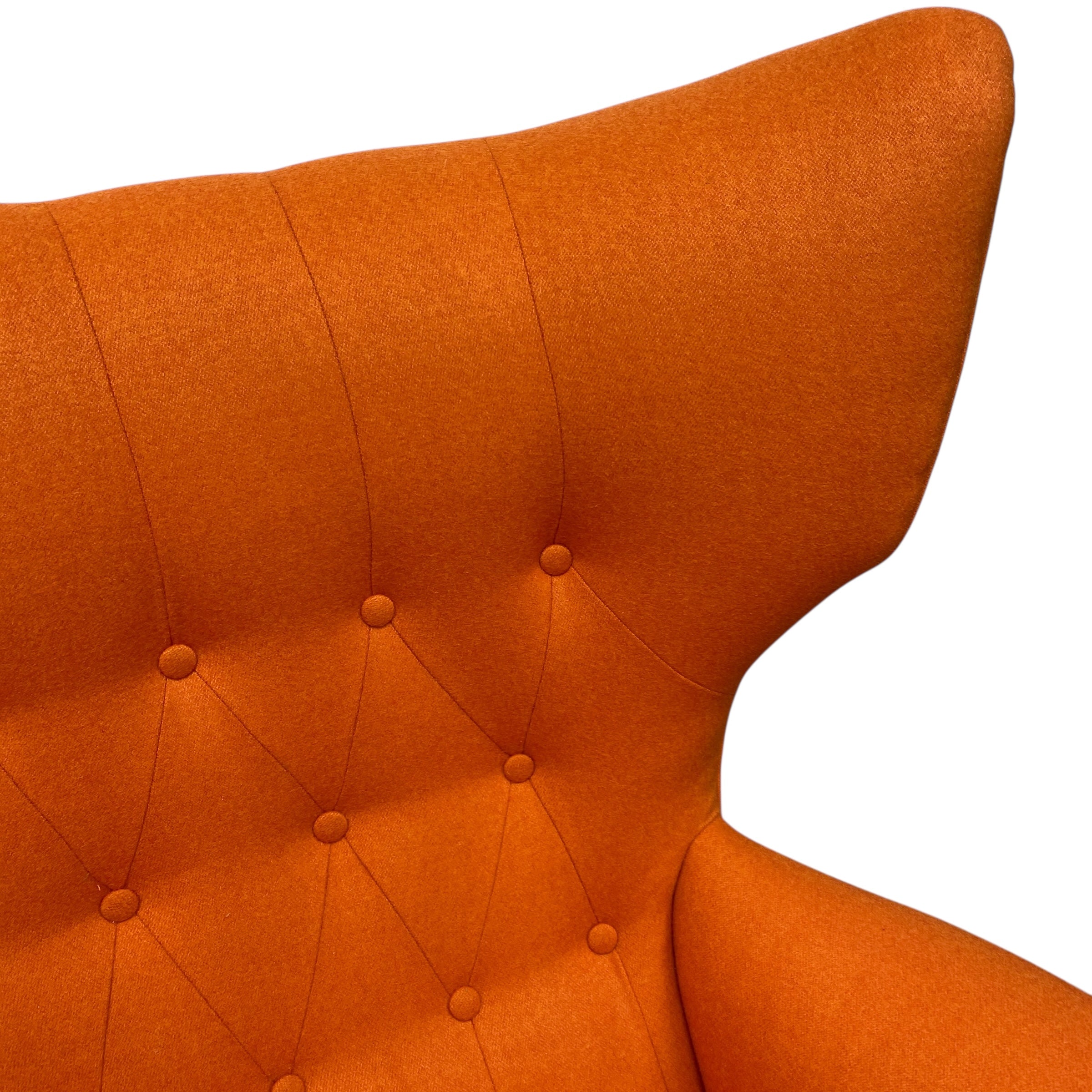 Close-up of an orange upholstered chair with button tufting on a white background