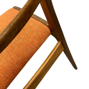 Close-up of an orange upholstered chair with wooden legs on a white background