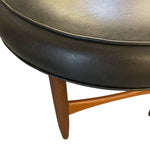 Load image into Gallery viewer, Round black leather ottoman with wooden legs on a white background
