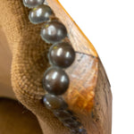 Load image into Gallery viewer, Close-up of a wooden shoe with a textured surface and a string of dark beads.

