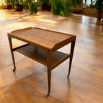 Load image into Gallery viewer, Wooden side table on wheels in a room with wooden flooring and plants.
