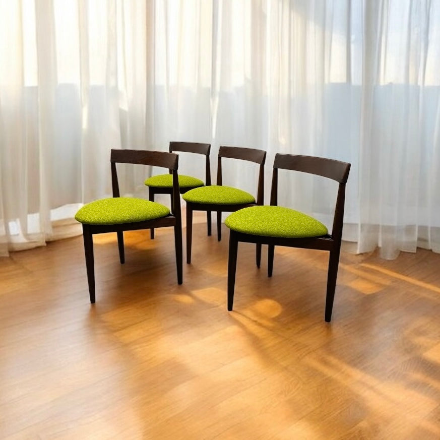 Four chairs with green cushions on a wooden floor in front of white curtains.