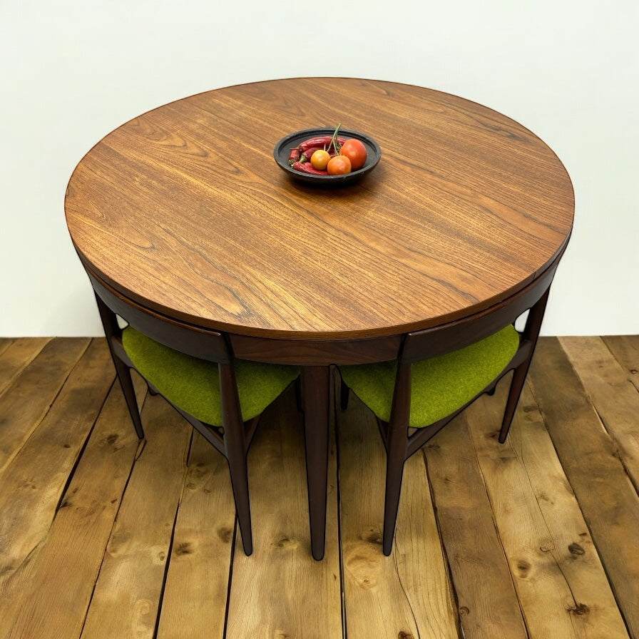 Round wooden table with green cushioned chairs on a wooden floor.