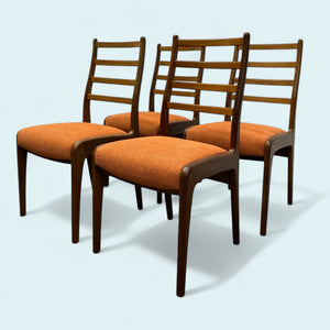 Four wooden chairs with orange seats on a light blue background