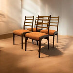 Load image into Gallery viewer, Four wooden chairs with orange cushions arranged in a room with beige walls and floor.
