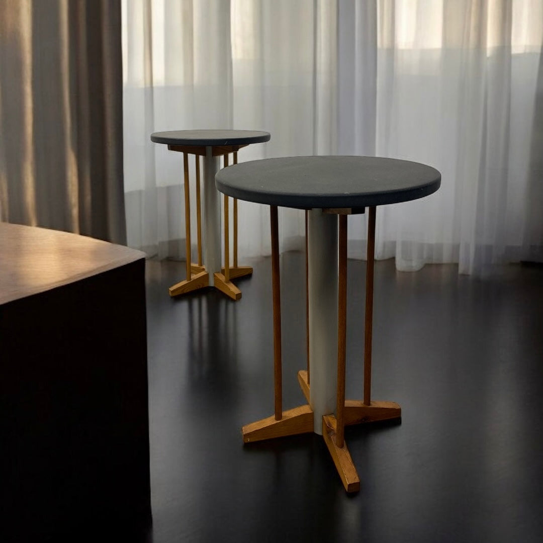 Two round tables with wooden legs on a dark floor with light filtering through curtains.