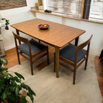 Load image into Gallery viewer, Wooden dining table with two chairs in a room with a window and plants.
