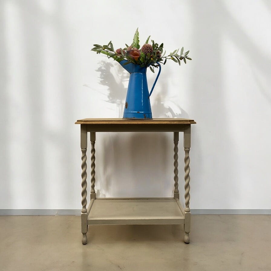 Wooden side table with a blue pitcher and floral arrangement against a white wall.