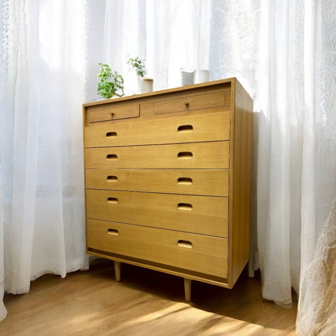 Wooden dresser with multiple drawers in a room with white curtains.