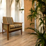 Load image into Gallery viewer, Brown armchair with striped cushions in a room with wooden floor and plant
