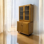 Load image into Gallery viewer, Wooden cabinet with glass doors in a room with curtains and a light-colored floor.
