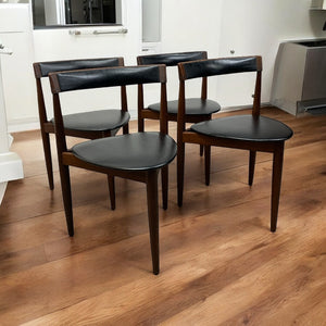 Four dark wooden chairs with black seats on a wooden floor.