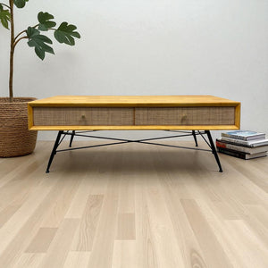 Wooden coffee table with woven design in a room with a plant and books.