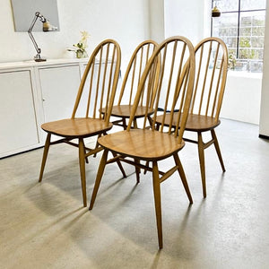 Set of four wooden chairs in a room with a desk and lamp.