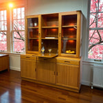 Load image into Gallery viewer, Wooden cabinet with glass doors in a room with cherry blossom trees outside.

