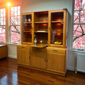 Wooden cabinet with glass doors in a room with cherry blossom trees outside.