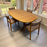Load image into Gallery viewer, Wooden dining table with four chairs in a room with large windows.
