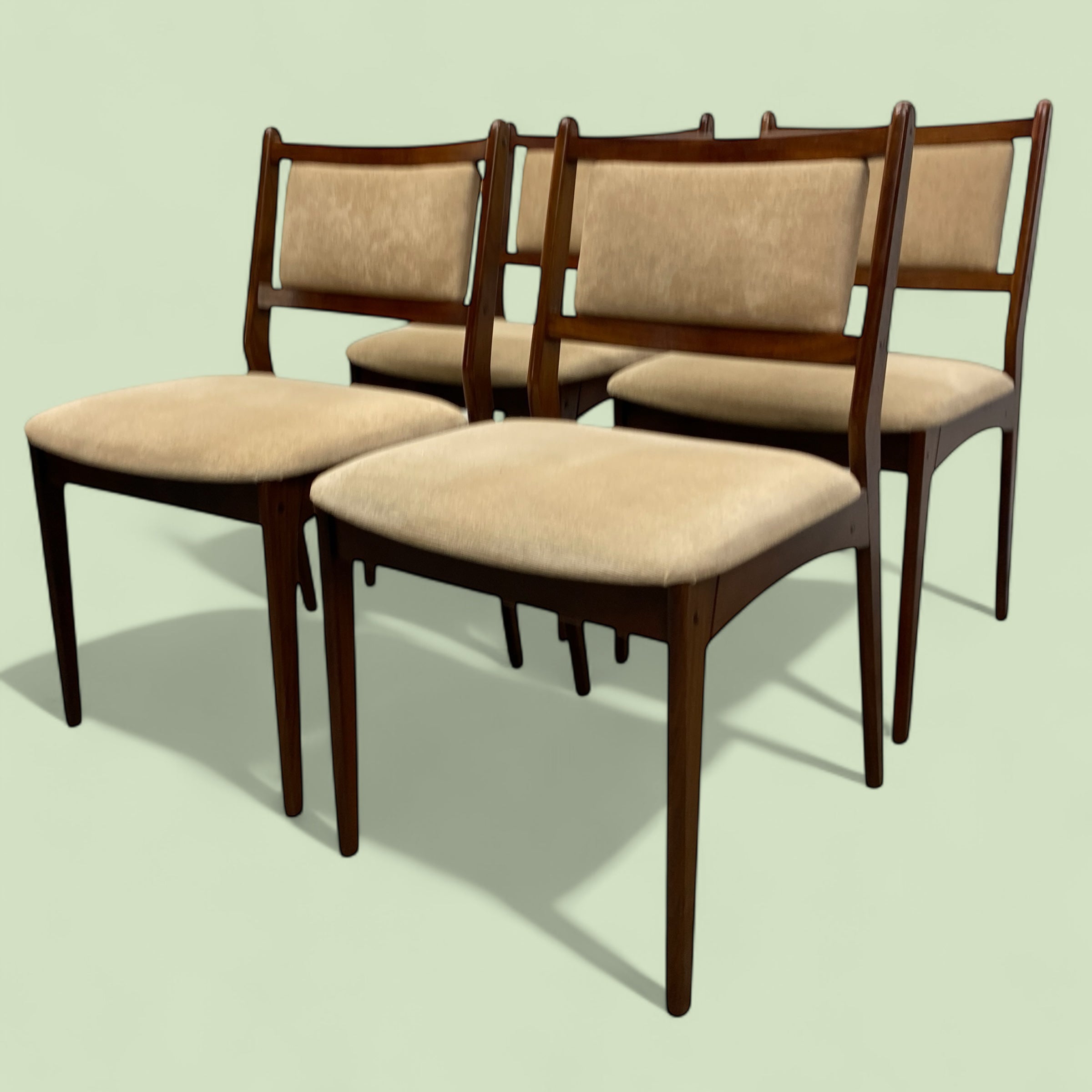 Set of four wooden chairs with beige cushions on a light green background