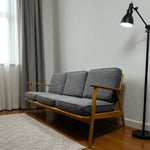 Load image into Gallery viewer, Grey sofa with wooden frame in a room with a lamp and curtains.
