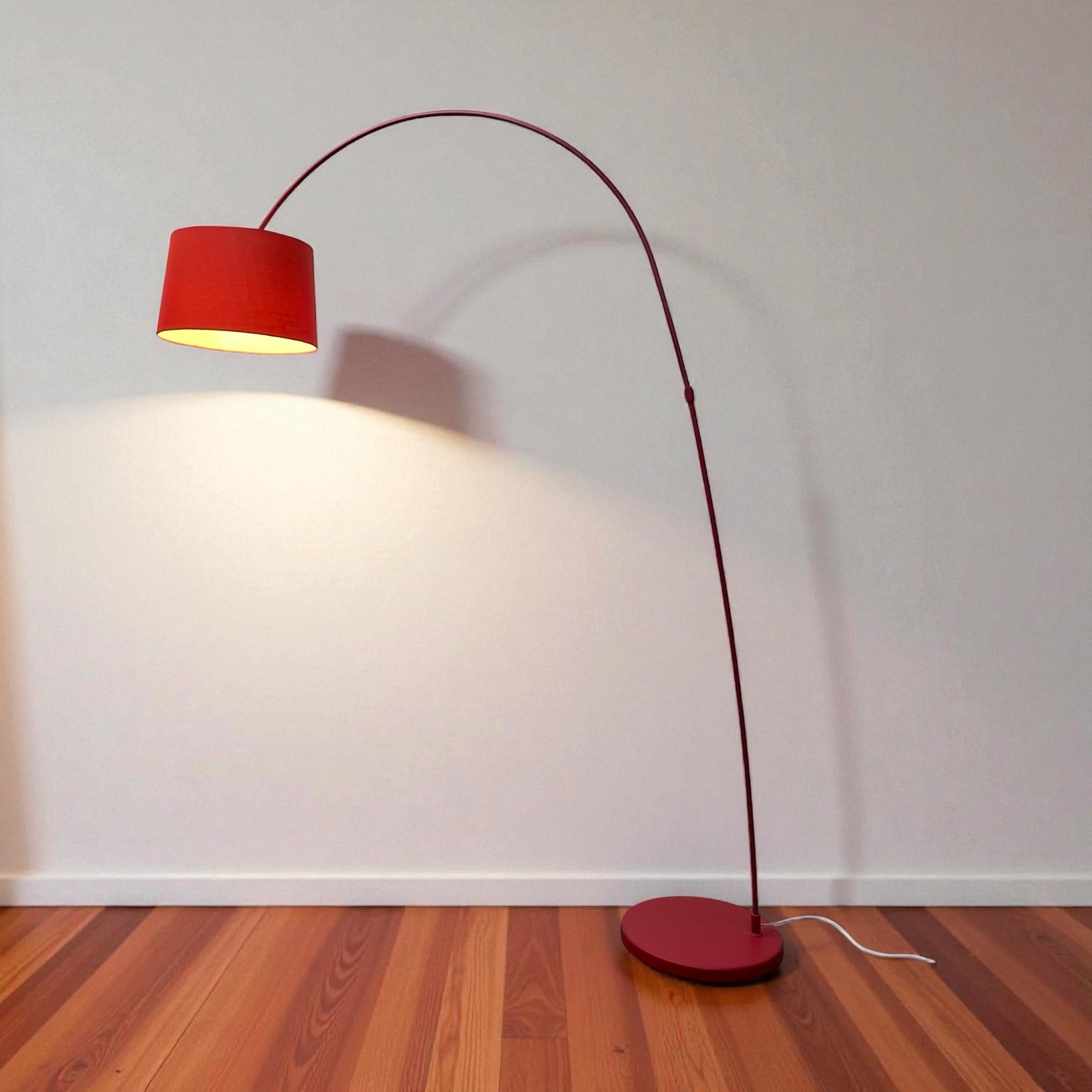 Red floor lamp with a red shade on a wooden floor against a white wall