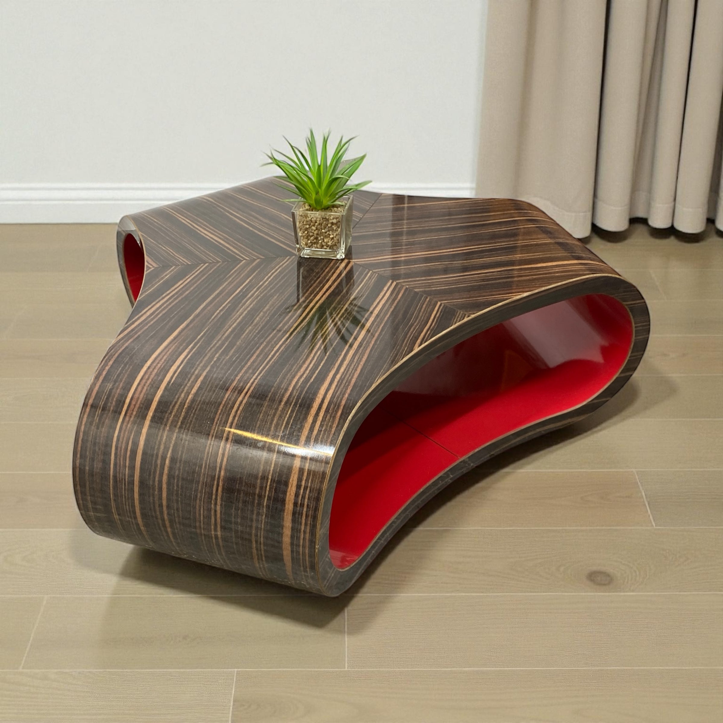 Modern coffee table with red interior and wavy design on a wooden floor.