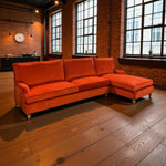 Load image into Gallery viewer, Orange sectional sofa in a room with brick walls and large windows.
