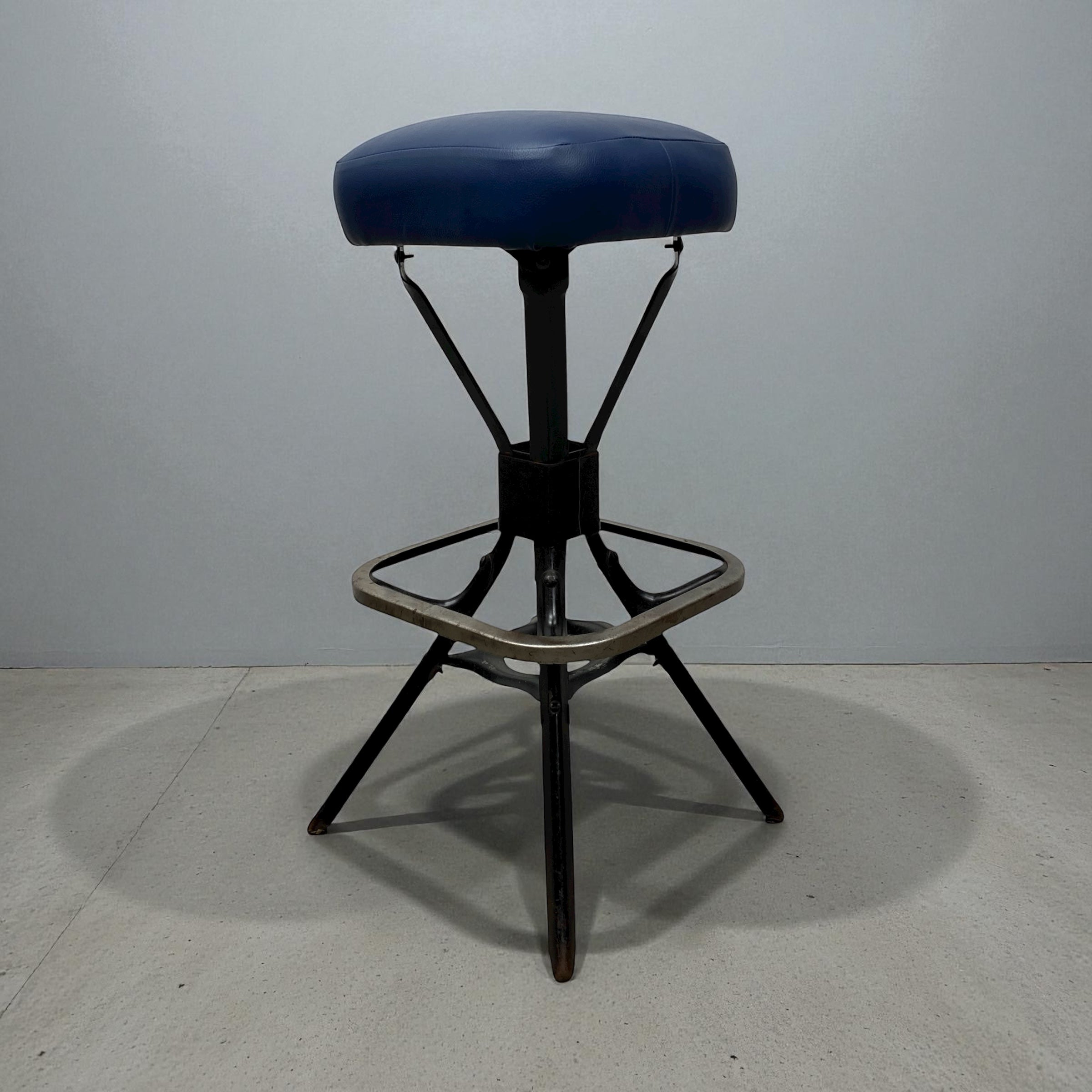 Blue cushioned stool with black metal frame on a gray floor and background